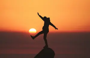 person posing on a rock, backlit by a setting sun